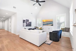 Un salon spacieux avec un canapé blanc, un pouf noir et un ventilateur de plafond.