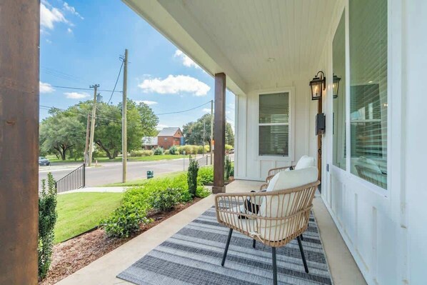 A porch with a chair and a rug, a street view, and a building in the background. - White Retreat- 3 King Suites! (Waco)