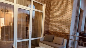 Varanda com mobiliário de vime, incluindo um sofá e uma mesa pequena, e uma parede de tijolos.