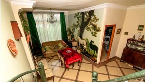 Uma sala de estar com sofá, uma mesa de jantar com toalha vermelha, escada e um mural de cavalos na parede.
