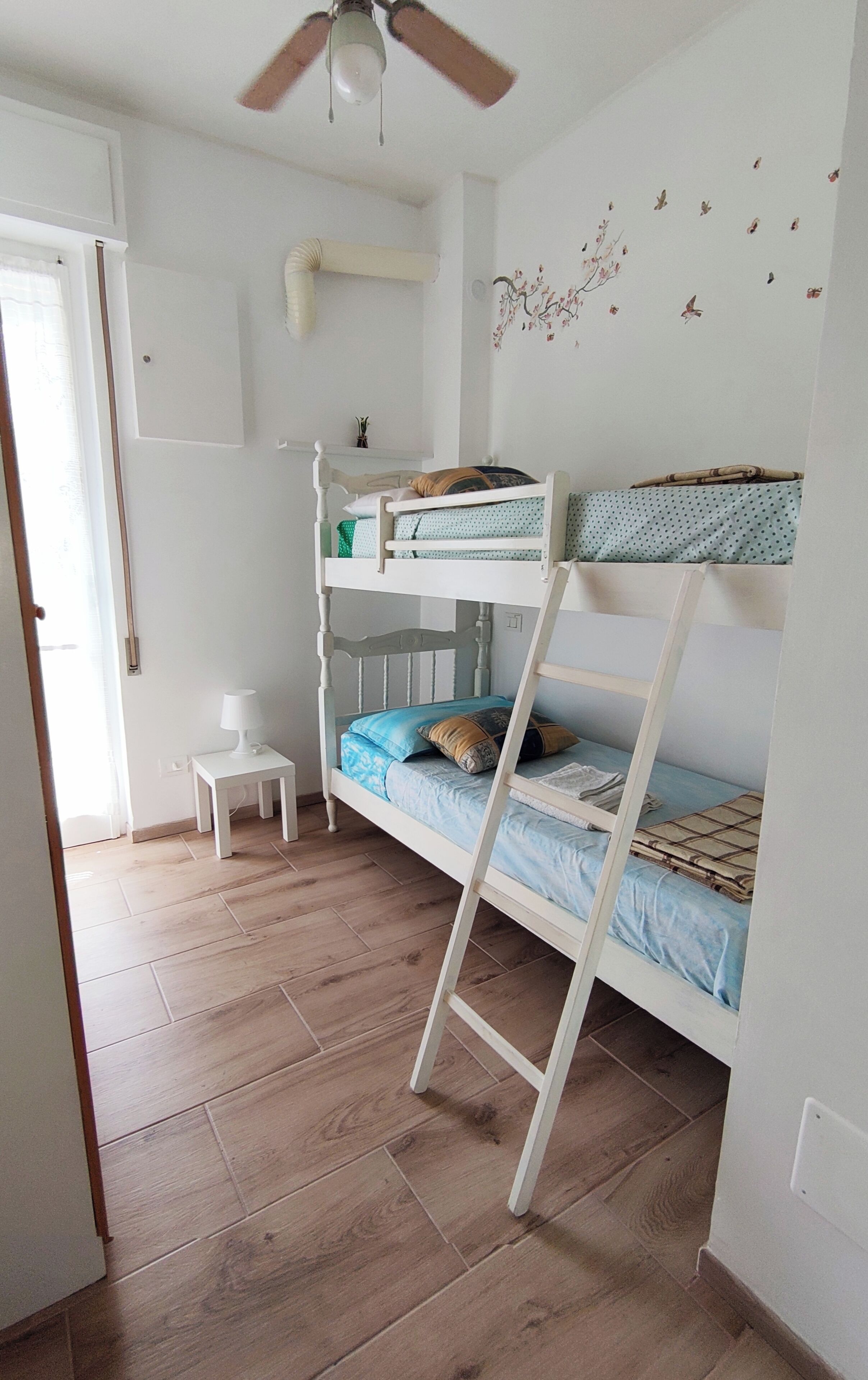 A bunk bed room with a ceiling fan, a small table, and a wall decal.
