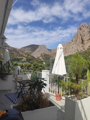 A balcony with a view of mountains, a table, chairs, and potted plants. - Elnidodelchorro  (Álora)