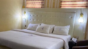 Una habitación de hotel con una cama grande, cabecera con diseño acolchado, dos lámparas de noche y una mesita con un teléfono.