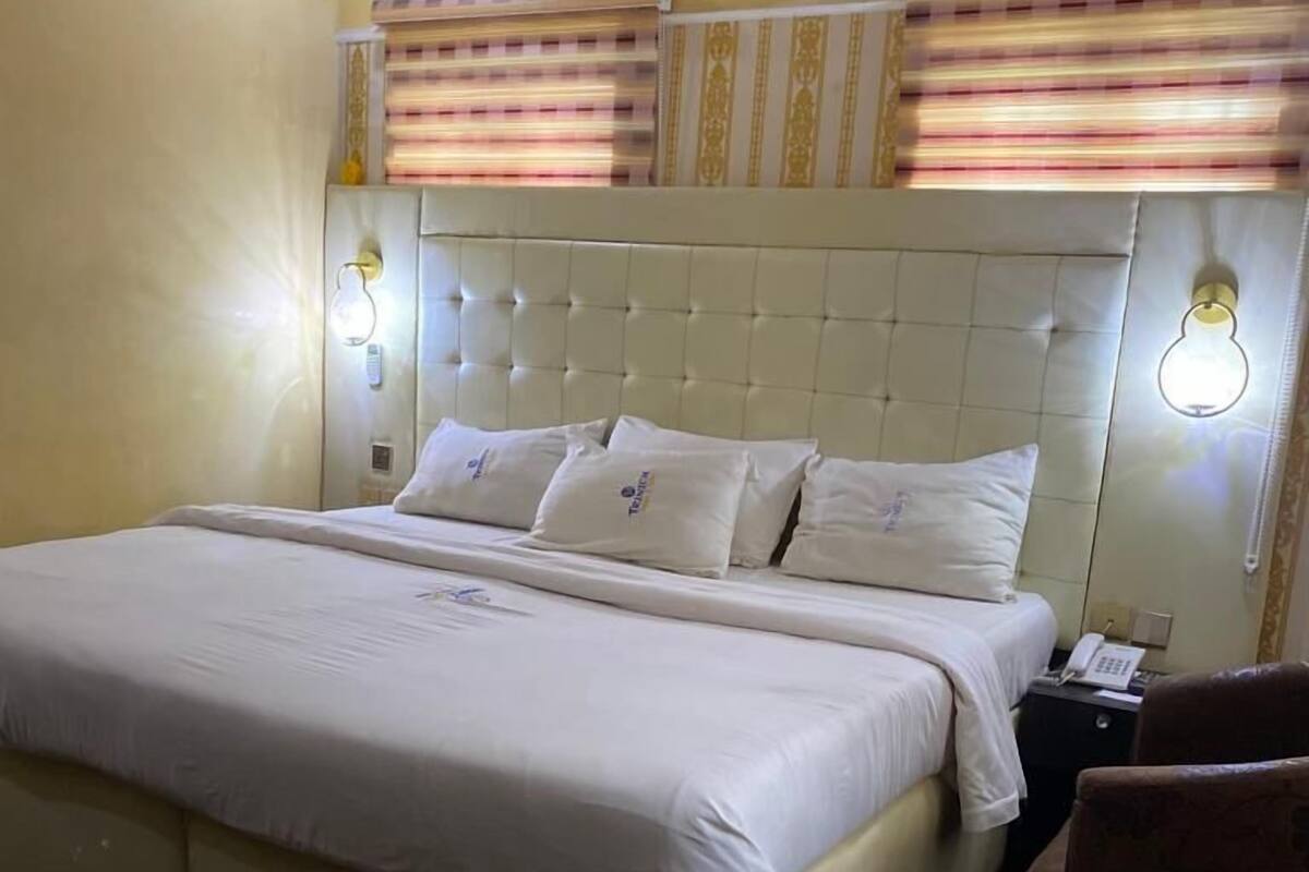 Una habitación de hotel con una cama grande, cabecera con diseño acolchado, dos lámparas de noche y una mesita con un teléfono.