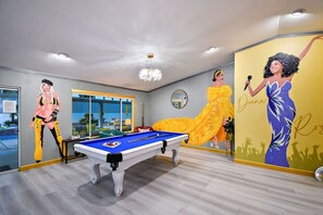 Una habitación con mesa de billar, un ventanal grande y un mural de una mujer con vestido.