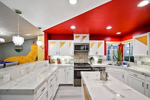 A modern kitchen with white cabinets, a central island, and a red accent wall.