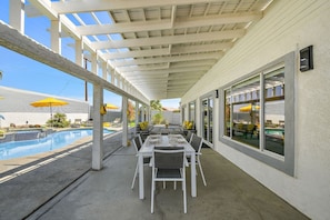 An outdoor patio with a pool, white furniture, and yellow umbrellas.