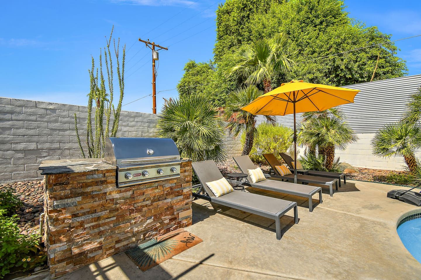 Une terrasse extérieure équipée d’un barbecue, de chaises longues et d’une piscine.