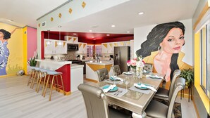 A modern kitchen with a central island, bar stools, and a dining area with a glass table and chairs. - Rock N Royalty: Pool, Spa, Fire Pit, Pool Table! (Bermuda Dunes)