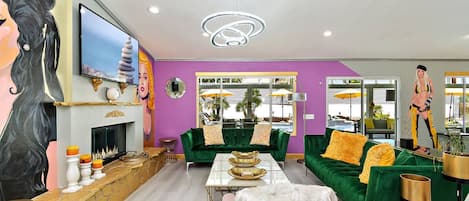 A modern living room with a fireplace, green sofas, a pink armchair, and a television.