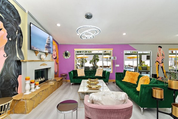 A modern living room with a fireplace, green sofas, a pink armchair, and a television.