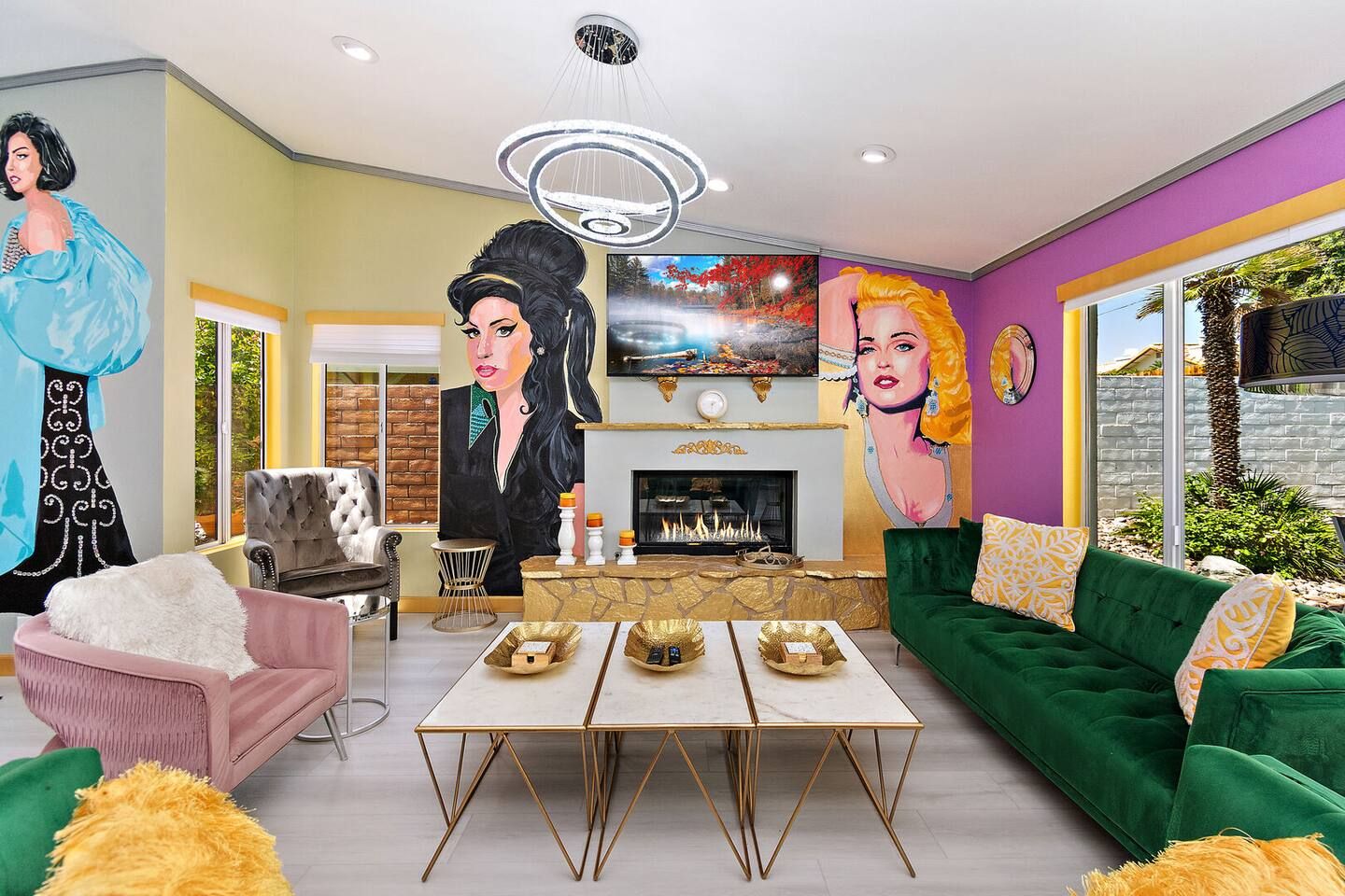 Un salon moderne avec une cheminée, des canapés verts, un fauteuil rose et un grand tableau représentant une femme.