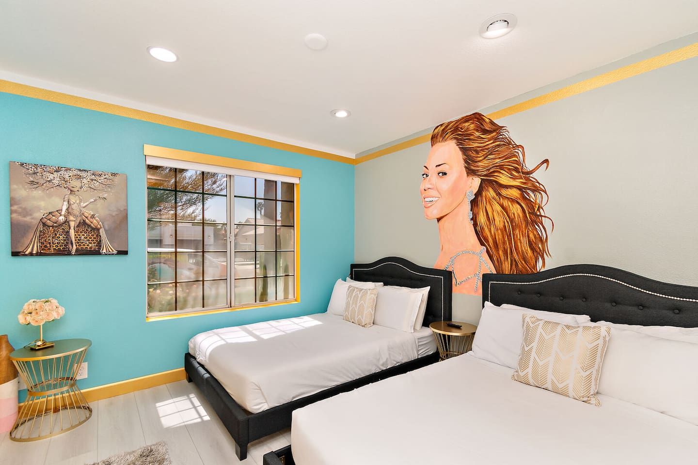 A bedroom with two beds, a large window, and artwork on the walls.