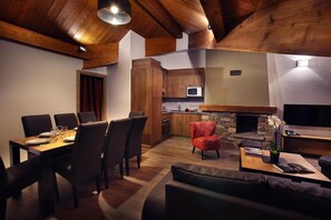Un comedor con una mesa y sillas de madera, una cocina con chimenea de piedra y una sala de estar con un sillón rojo y un sofá.
