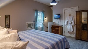 Un dormitorio con cama, televisor, armario y ventana con cortinas.