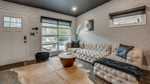 A modern living room with a tufted sofa, a round coffee table, and a large window with a view. - Modern Atlanta Retreat: Private Hot Tub & Yard! (Atlanta)
