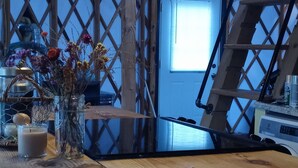 An attic-style room with exposed wooden beams, a wooden table, hanging light fixtures, and a window with blinds. - Madison's Only YURT Experience  (Madison)