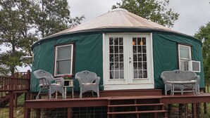 A green yurt with a white door and windows, a covered porch with wicker chairs, and a wooden staircase leading up. - Madison's Only YURT Experience  (Madison)