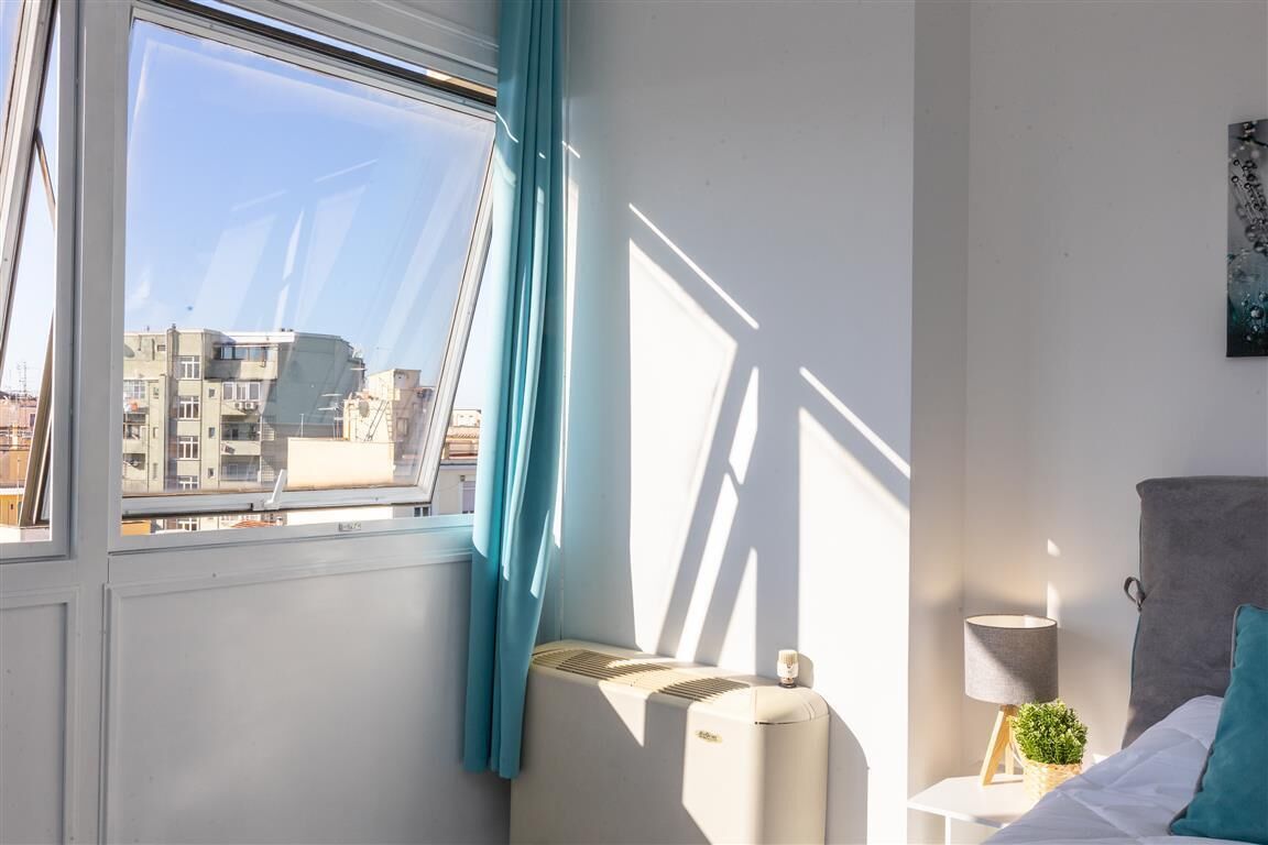 Ein Hotelzimmer mit großem Fenster, Heizkörper, Nachttischlampe und einem Bett mit Kissen.