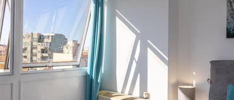 Ein Hotelzimmer mit großem Fenster, Heizkörper, Nachttischlampe und einem Bett mit Kissen.