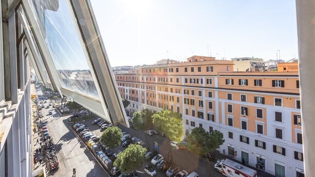 Une vue depuis un immeuble de grande hauteur, donnant sur une rue de la ville, avec des voitures garées et d’autres immeubles.
