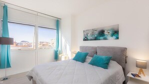 Une chambre d’hôtel moderne avec un grand lit, un tableau au mur et une vue sur la ville par les fenêtres.