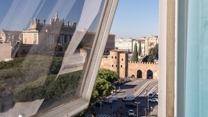 Une vue à travers une fenêtre sur un paysage urbain caractérisé par une architecture historique, notamment un bâtiment imposant orné de statues et surmonté d’une grande arche.