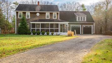 A two-story house with a covered porch, a garage, and a gravel driveway.