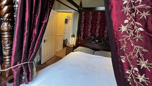 Une chambre à coucher avec un lit à baldaquin, une tête de lit en bois et une grande fenêtre avec des rideaux.