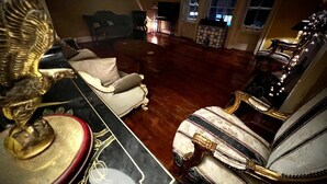 Une pièce dotée d’un plancher en bois, d’un grand lampadaire décoratif et de deux fauteuils rembourrés ornés de motifs dorés.