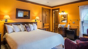 A hotel room with a large bed, two bedside lamps, a mirror, a bathroom with a sink and mirror, and a window with curtains.