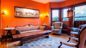 A room with a sofa, armchairs, a wooden coffee table, a clock, and a painting on the wall.