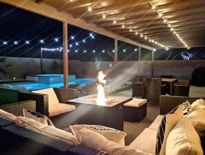 Ein Außenbereich zum Entspannen mit Feuerstelle, Sitzgelegenheiten und Blick auf einen Pool.
