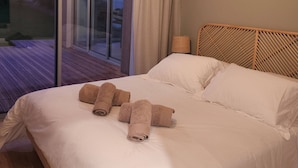 A bedroom with a large bed, a wooden headboard, and a view through a glass door to an outdoor deck. - Villa with indoor pool 5 minutes walk from the beach (Plouguerneau)