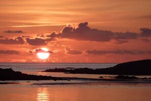 Un atardecer sobre una costa rocosa con aguas tranquilas que reflejan el cielo.