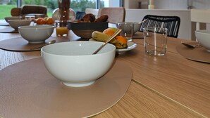 A modern dining area with a wooden table, white bowls, and a vase with branches. - Villa with indoor pool 5 minutes walk from the beach (Plouguerneau)