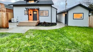 Une maison à deux étages avec un porche à l’avant, un petit garage attenant et une pelouse bien entretenue.