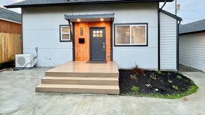 Une maison moderne à deux étages, avec une porte d’entrée sombre, un petit porche et une allée en béton.