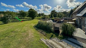 A sunny outdoor area with a playground, a wooden deck, and a stone building.
