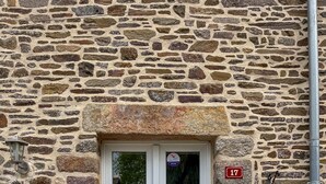 A stone building with a white door, a doormat with "home" written on it, and a number plate "17" on the wall.