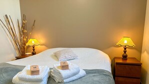 A neatly made bed with white linens, two bedside lamps, a bedside table, and a decorative branch arrangement.
