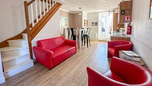A spacious living room with a wooden staircase, red leather sofas, and a dining area with black chairs.