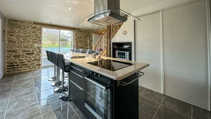 Eine moderne Küche mit einer zentralen Kochinsel, schwarzen Schränken, einem eingebauten Ofen und einer Wand mit Steinverkleidung.