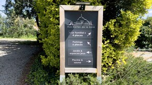 A directional sign with arrows pointing to various amenities including 'Le Familial' with 4 places, 'Parkings' with 6 places, 'Jardin & espaces jeux', and 'Piscine & sauna'.