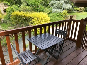 Eine Holzterrasse mit Tisch und Stühlen, umgeben von üppiger Vegetation und Gartenblick.