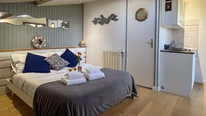 A bedroom with a bed, a small kitchenette, a radiator, and a door with a round mirror.