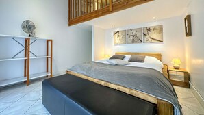 Ein Schlafzimmer mit einem Bett, einer hölzernen Bank, einem Ventilator und Kunstwerken an der Wand.