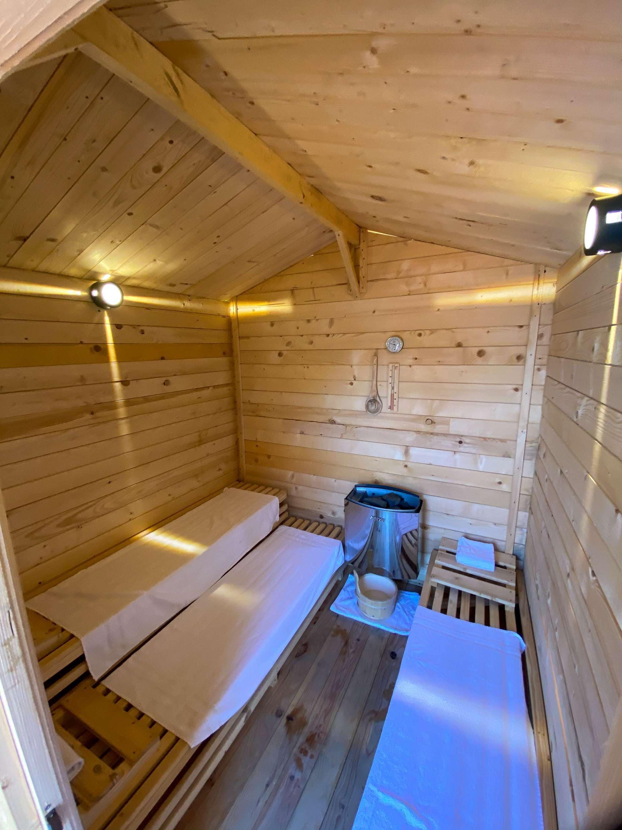 A small wooden cabin with two beds, a heater, and a thermometer on the wall.