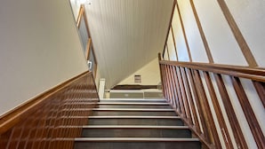 Eine Treppe mit Holzhandläufen und dunklen Fliesenstufen, die zu einer Zwischenebene mit einem Schild führt.
