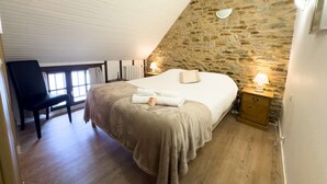 Ein Schlafzimmer mit Steinsandsteinwand, einem Bett mit beiger Bettdecke, einem Nachttisch mit Lampe und einem Schreibtisch mit Stuhl.